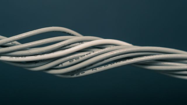 A bundle of grey electrical wires, slightly twisted around each other, in front of a dark blue background. 