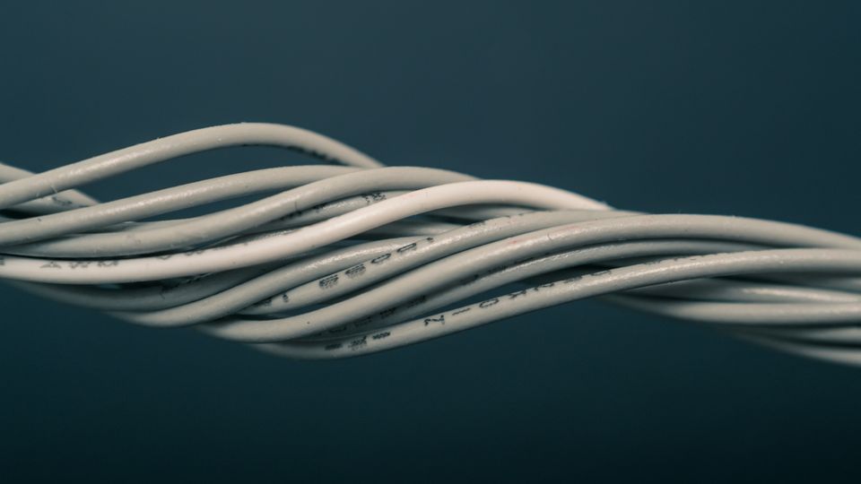 A bundle of grey electrical wires, slightly twisted around each other, in front of a dark blue background.