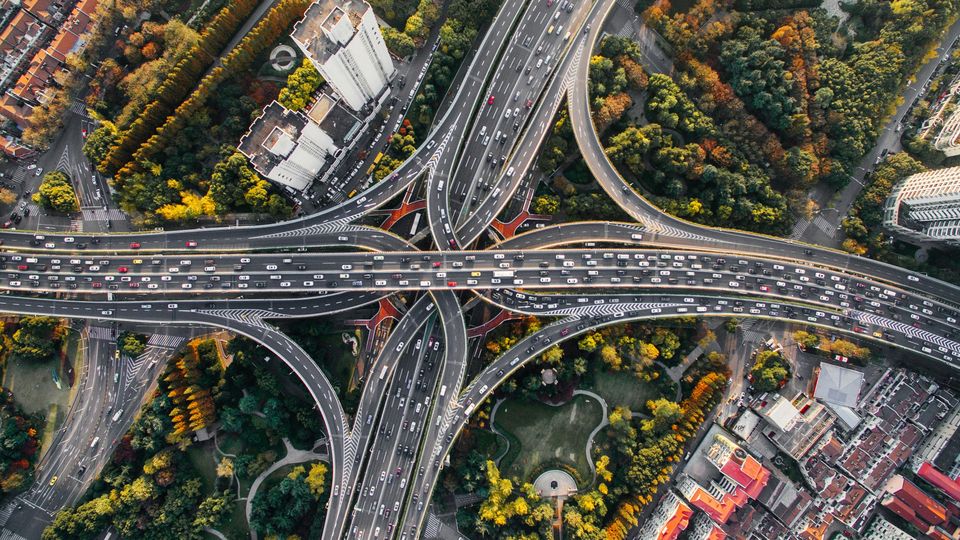 An aerial photo of a complex highway interchange in a city, surrounded by tall buildings and green trees.