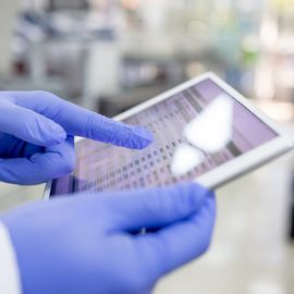 Gloved scientist using a tablet to access LIMS data in a modern laboratory setting. 