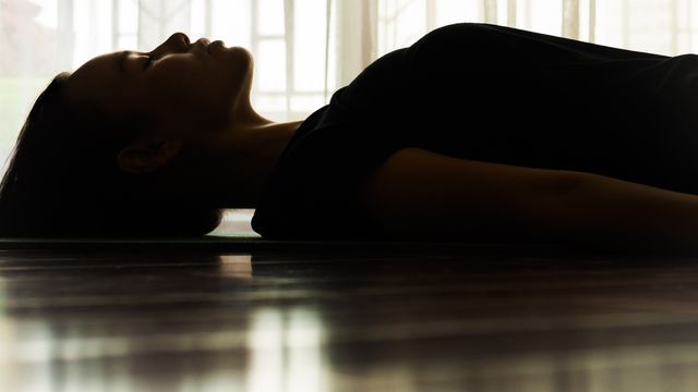 Person lying still in a dimly lit room, symbolizing therapeutic use or effects of MDMA. 