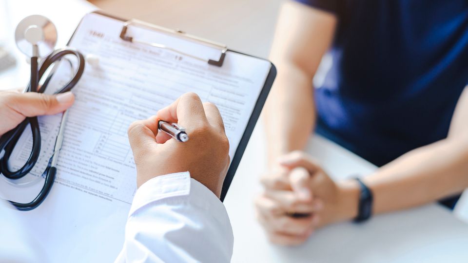 Doctor filling out a diagnostic form during a patient consultation in a clinical setting.