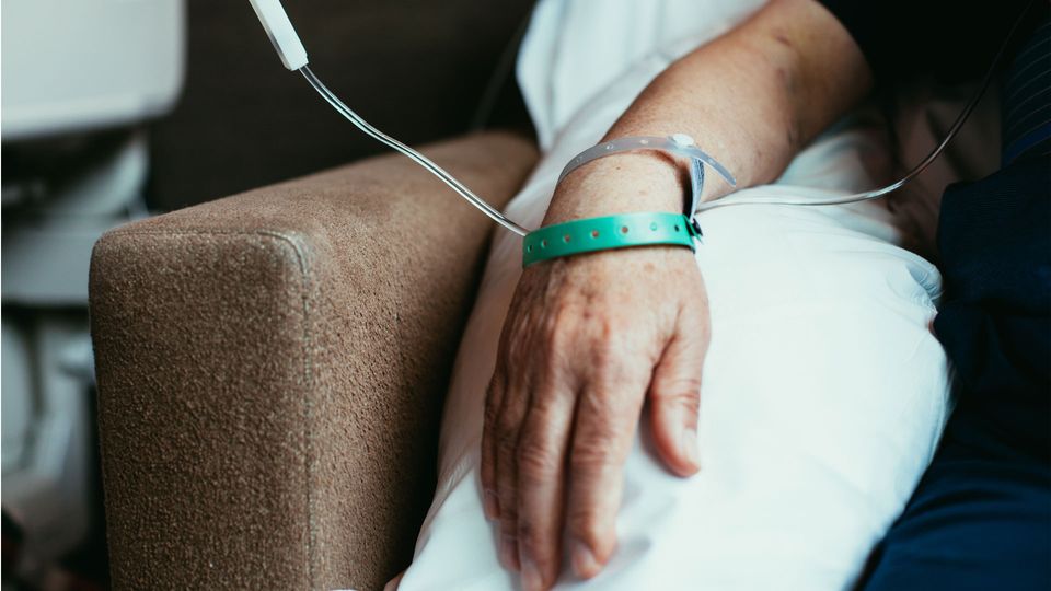 A cancer patient's arm and hand, with a tube carrying cancer therapy coming across their body.