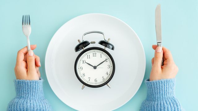Clock on a plate with utensils symbolizing the concept of intermittent fasting and meal timing. 