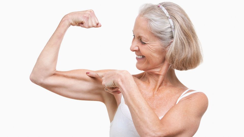 Fit senior woman smiling and flexing her arm, symbolizing strength and healthy longevity.