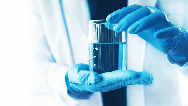 Lab technician holding beaker of solution. 
