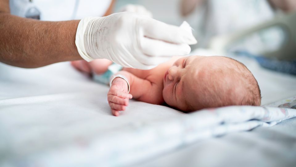 Newborn baby receiving care from a gloved medical professional after a C-section delivery.