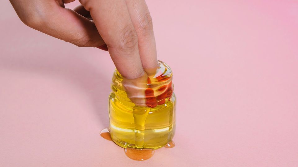 Hand dipping fingers into a small jar of oil, symbolizing self pleasure and intimate self-care.