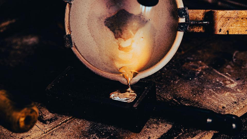 Molten metal being poured from crucible during metal processing.