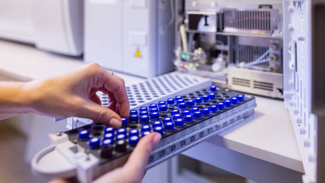 Researcher loading sample vials into a mass spectrometry machine for chemical analysis. 