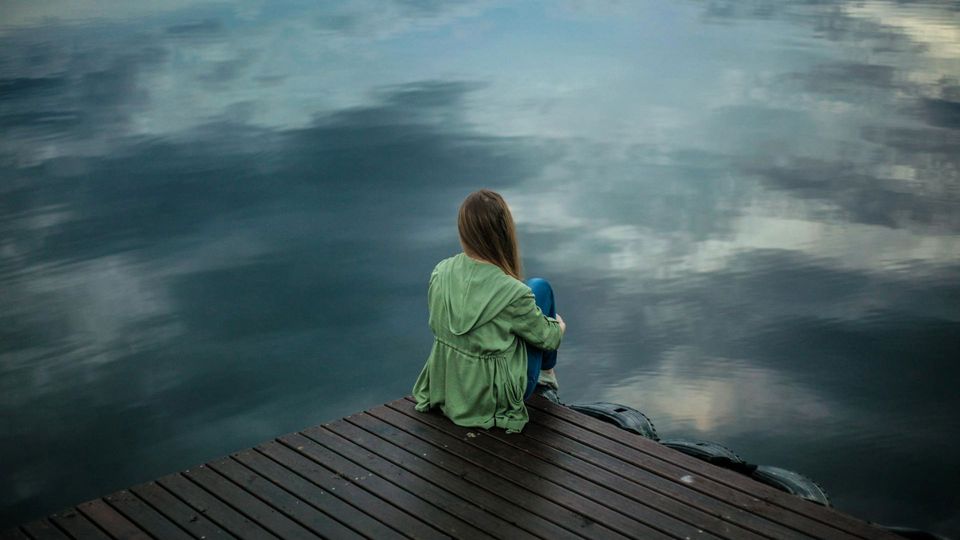 A woman sits on a dock overlooking a lake, illustrating sadness and depression.