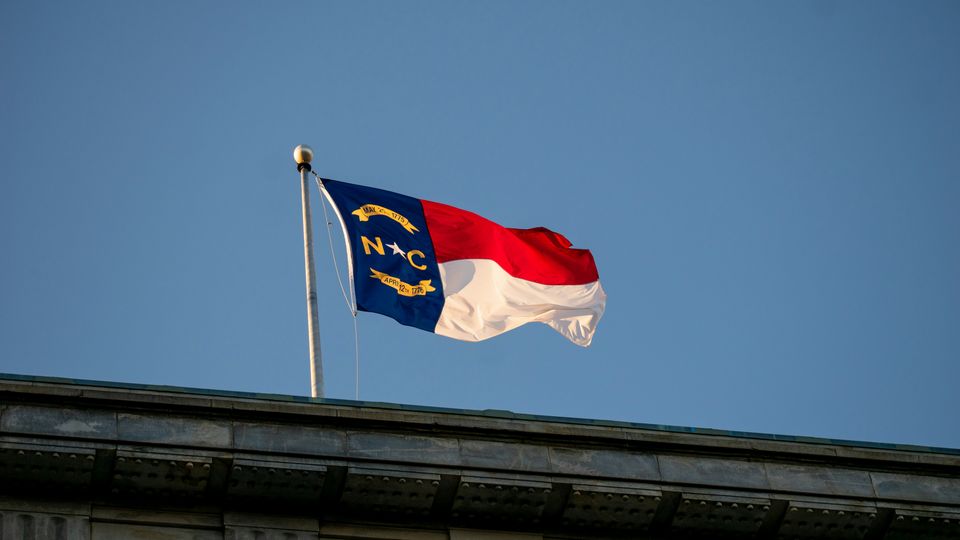 The North Carolina state flag flying over the edge of a stately building.