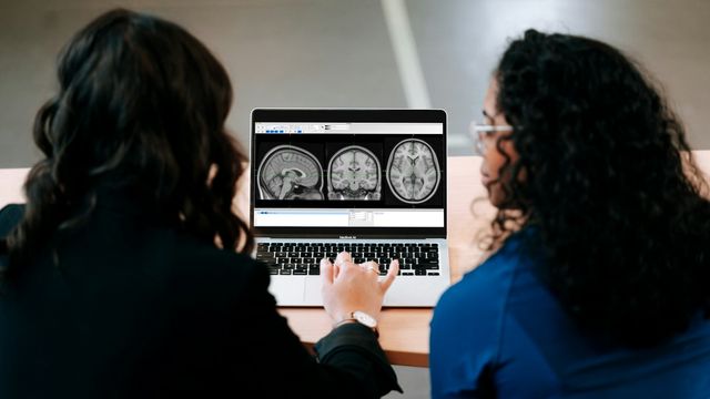 Researchers reviewing brain scan images on a laptop to illustrate progress toward dual-target CAR-T therapy for glioblastoma. 