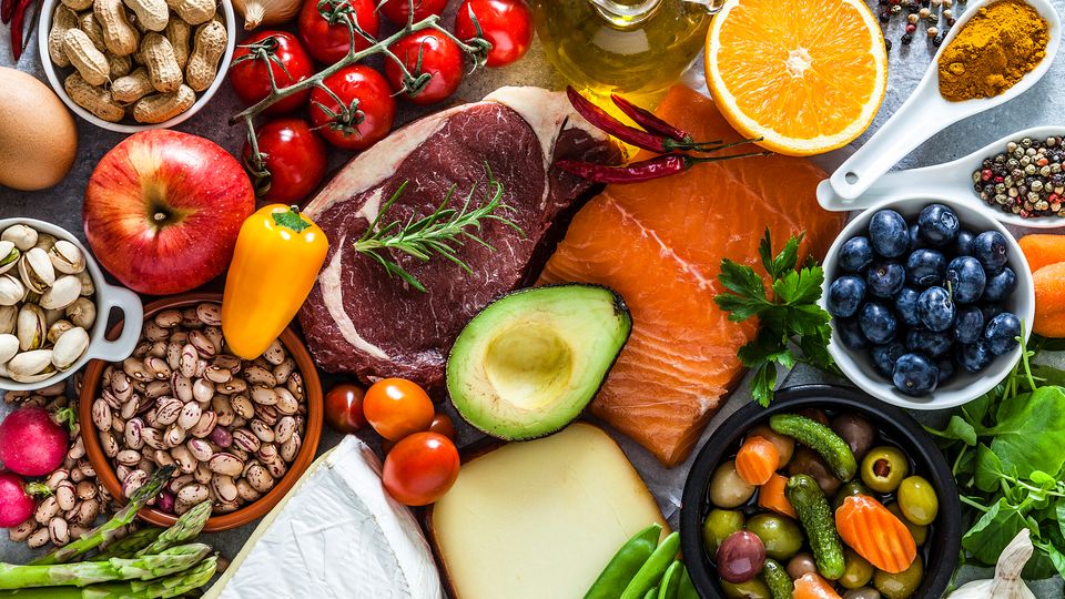Assortment of fresh whole foods including fruits, vegetables, meats and grains, contrasting ultra-processed diets.