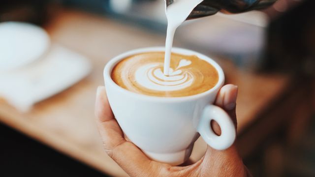 Milk being poured into a cup of coffee to create latte art in a white ceramic mug. 