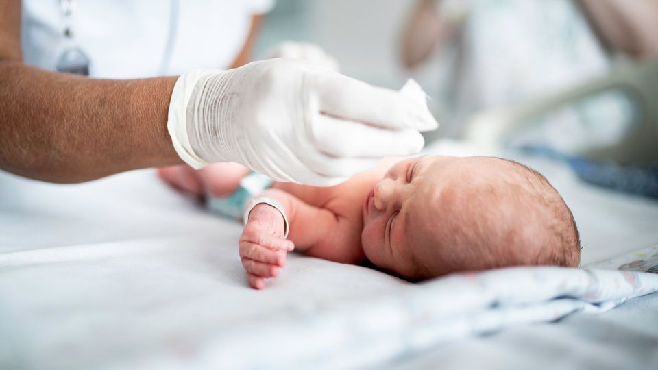 Gloved healthcare worker gently caring for a pre-term baby lying on a hospital bed.