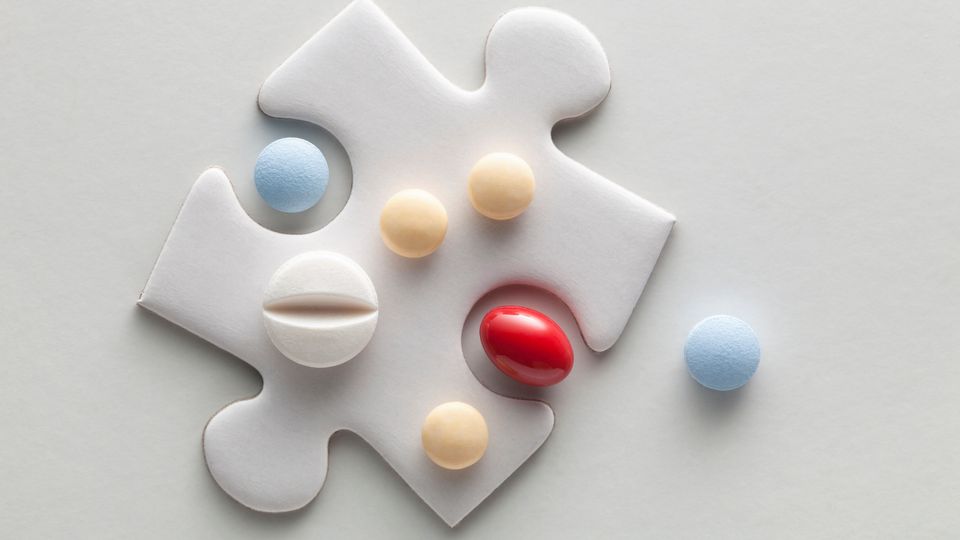 A variety of colorful pills arranged on top of a white puzzle piece, symbolizing medical treatment or pharmaceutical research.