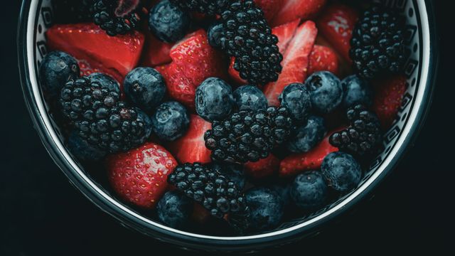 A close-up photo of a ceramic bowl containing chopped strawberries, blackberries and blueberries. 