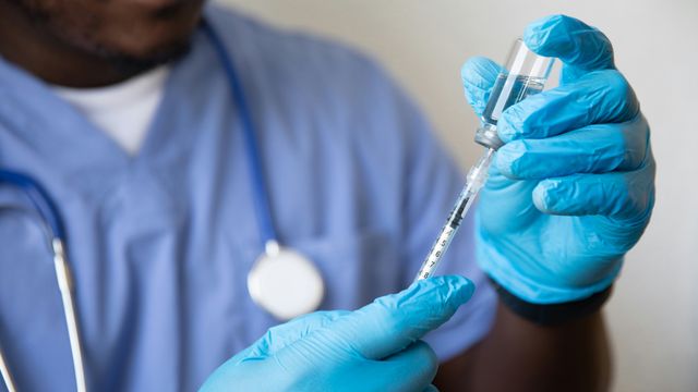 A nurse in blue gloves drawing medicine from a vial into a syringe. 