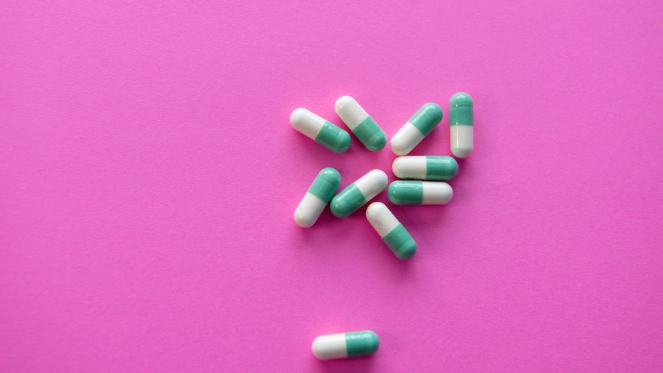 White and turquoise pills on a pink background.