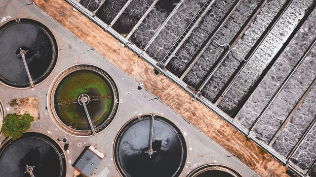 An aerial photo of a wastewater treatment plant, featuring long straight channels of water as well as circular treatment tanks. 