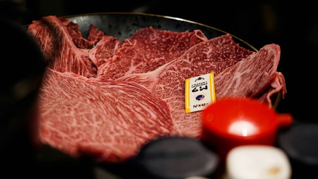 Slices of Wagyu beef on a dark blue plate. Several jars of spices are out-of-focus in the bottom-right corner. 