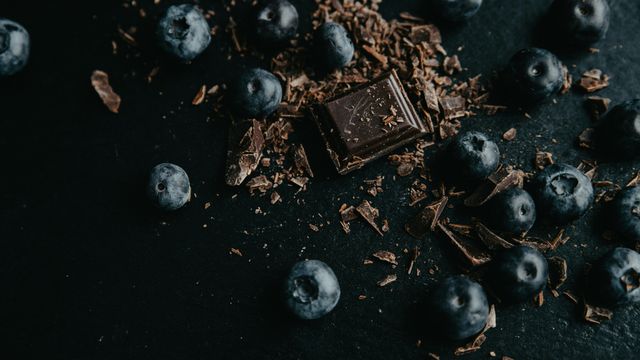A square of dark chocolate and chocolate shavings, surrounded by blueberries. 