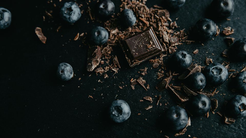 A square of dark chocolate and chocolate shavings, surrounded by blueberries.