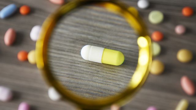 A magnified view of a yellow and white capsule among other medications, representing drug repurposing. 