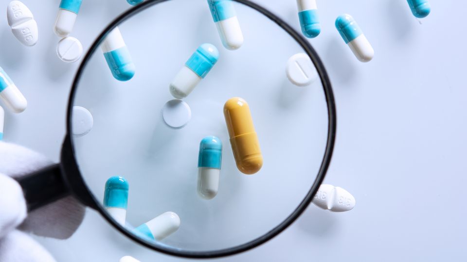 Magnifying glass highlighting a yellow capsule among white and blue metformin pills.