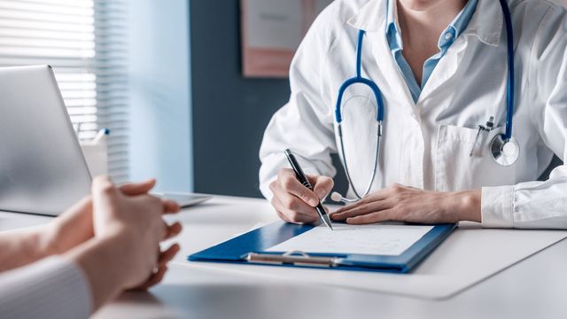 A doctor writing on a clipboard while speaking to a patient. 