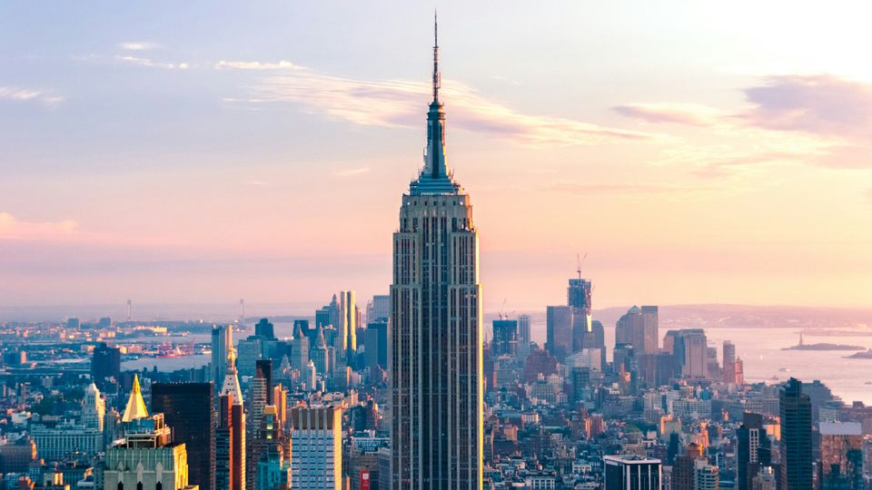 The Empire State Building against the New York skyline at sunrise.
