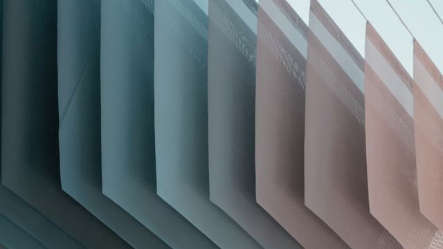 An abstract photo of many thin layers of material, colored on a gradient from blue on the left to light pink on the right. 