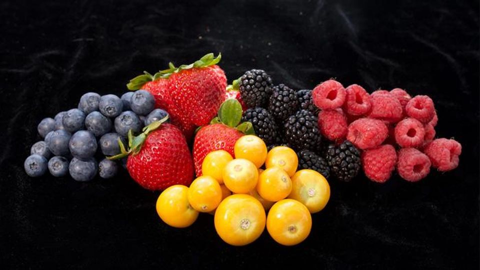 Assorted berries including goldenberries, strawberries and raspberries arranged on a black background.