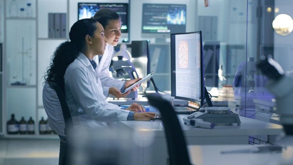 Laboratory scientists monitoring bioprocessing workflows and data on computer screens.