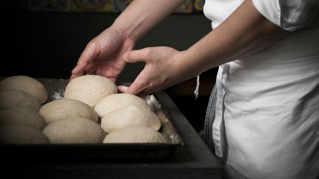 A baker in a white apron placing shaped bread rolls onto a tray for baking. 