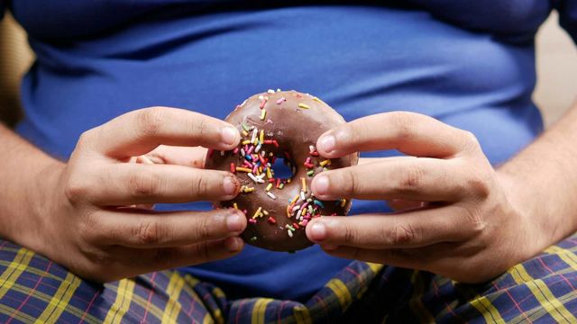 Hands holding a chocolate-frosted donut with sprinkles, illustrating processed food consumption. 