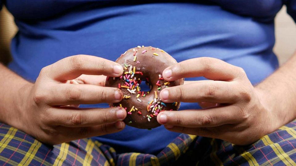 Hands holding a chocolate-frosted donut with sprinkles, illustrating processed food consumption.