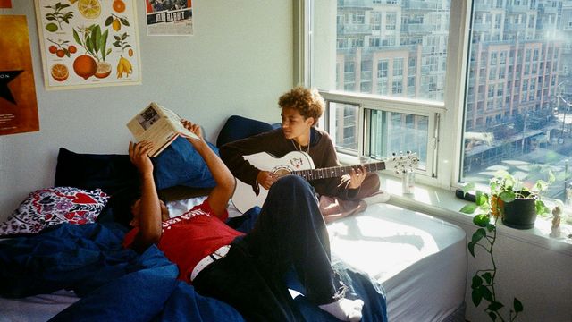 Two roommates relaxing in a sunlit apartment bedroom. 