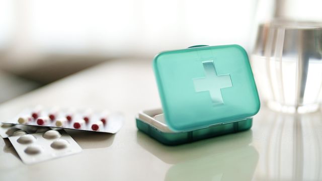 A green plastic medicine box placed next to blister packs of pills and a glass of water, suggesting medication management for chronic pain. 
