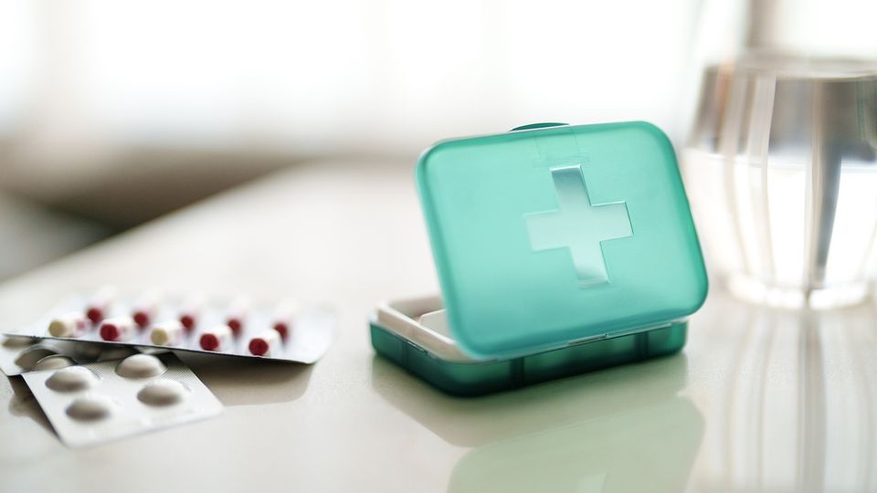 A green plastic medicine box placed next to blister packs of pills and a glass of water, suggesting medication management for chronic pain.