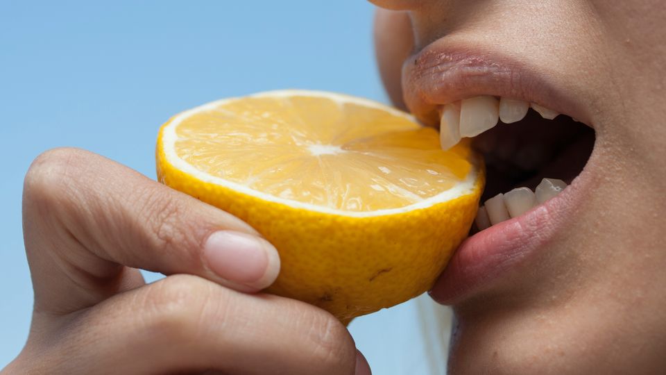 A woman biting into a slice of lemon.