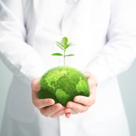 A scientist in a white lab coat holding a model of a green earth, representing lab sustainability. 