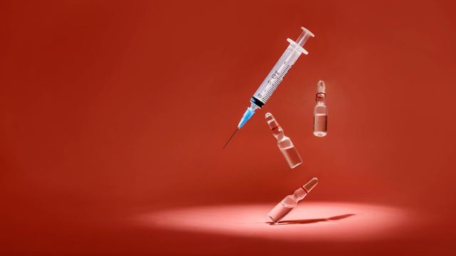 Syringe and three glass vaccine vials on a red background. 