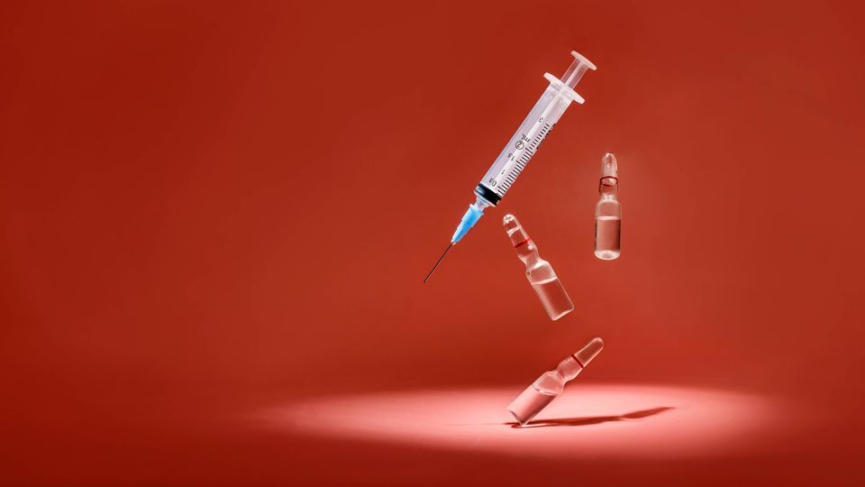 Syringe and three glass vaccine vials on a red background.