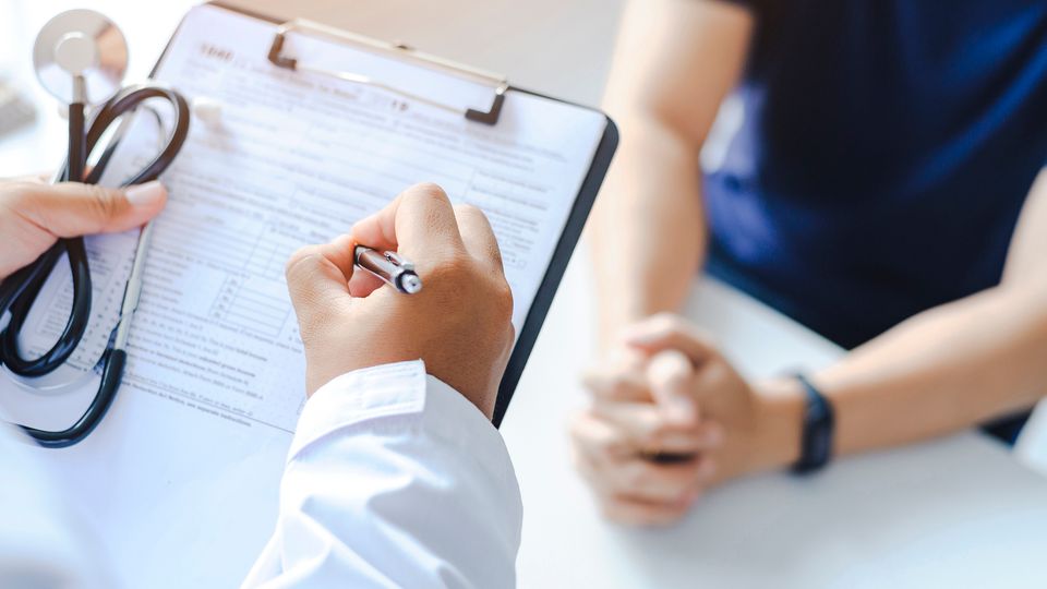 A doctor makes notes on their clipboard while speaking to a patient.