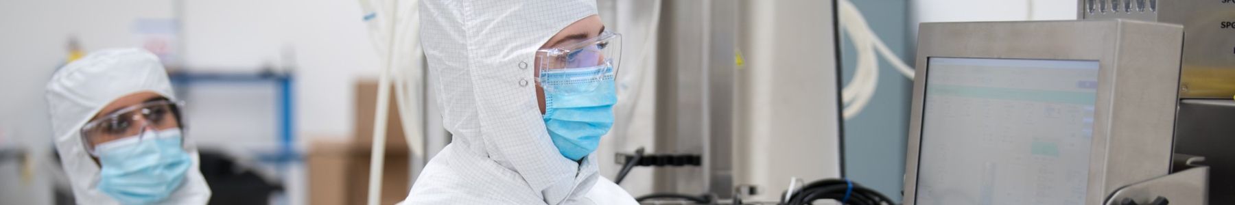 Scientist monitoring stainless steel bioreactor system for protein production in a cleanroom. 