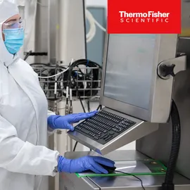 Scientist monitoring stainless steel bioreactor system for protein production in a cleanroom with Thermo Fisher Logo