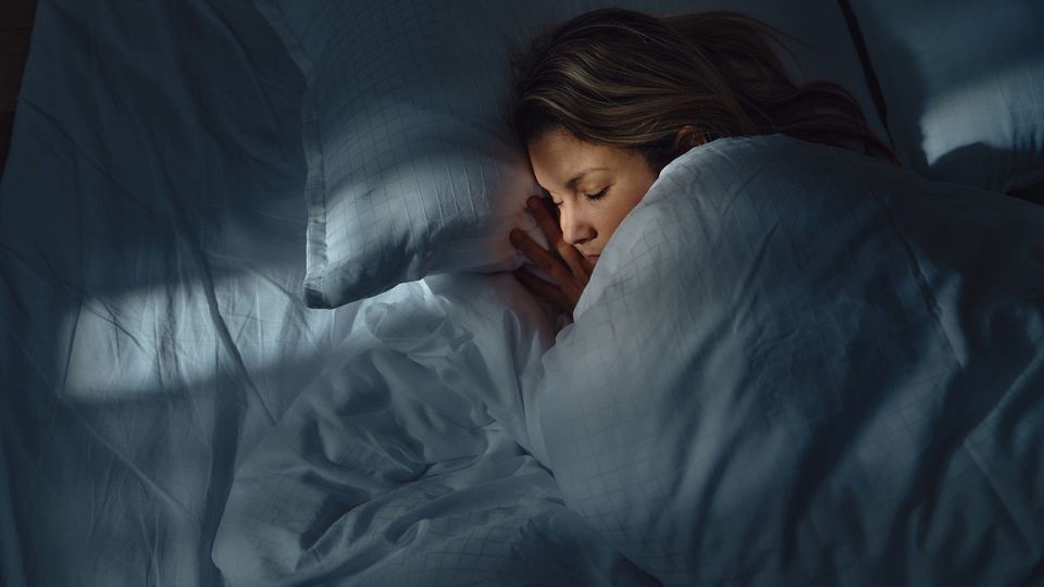 Woman peacefully sleeping in bed at night with soft natural light filtering through.