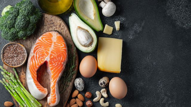 Flat-lay photograph of key components of the keto diet, including eggs, oily fish, avocadoes, nuts, and seeds. 